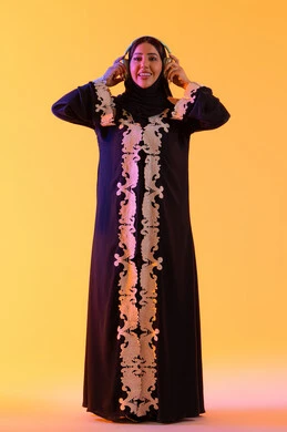 قضاء وقت ممتع بالاستماع الى الموسيقى, مفهوم الإصغاء والاستمتاع، سيدة اماراتية تستخدم الهيدفون في اوقات الفراغ، بورتريه لامرأة عربية خليجية سعودية ترتدي العباءة المطرزة والحجاب تضع سماعات الرأس بتعابير السعادة، تطور التقنيه والتكنولوجيا، خلفية صفراء