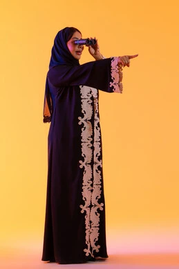 Pointing to something, seeing distant things and bringing them closer, a Saudi woman who loves exploration and adventure, a portrait of an Arab Gulf Emirati woman wearing an abaya and hijab, holding binoculars in her hand and looking with gestures of joy and enjoyment.