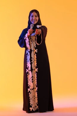 Practicing the talent of singing, a portrait of an Emirati Gulf Arab woman wearing an embroidered abaya and hijab holding a microphone in her hand, a Saudi woman singing with gestures of enthusiasm and joy, expressions of immersion and interaction with the music, presenting vocal performances, recording a singing audio clip, hosting radio programs, yellow background.