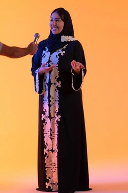 بورتريه لامراه عربيه خليجيه اماراتيه ترتدي العباءه المطرزة والحجاب تمسك بيدها المايكروفون ، سيده سعوديه تقدم اخبار عالميه متنوعه بإيماءات السرور، تعابير الاندماج والتفاعل ، تقديم العروض الصوتية ، العمل في تقديم الفقرات و البرامج الفنية الترفيهية، تقديم البرامج الاذاعية، خلفية صفراء