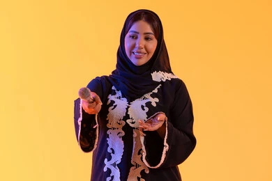 بورتريه لامراه عربيه خليجيه اماراتيه ترتدي العباءه المطرزة والحجاب تمسك بيدها المايكروفون ، سيده سعوديه تغني بإيماءات الحماس والسرور، تعابير الاندماج والتفاعل مع الموسيقي، تقديم العروض الصوتية ، تسجيل مقطع صوتي غنائي، تقديم البرامج الاذاعية، ممارسة موهبة الغناء،خلفية صفراء