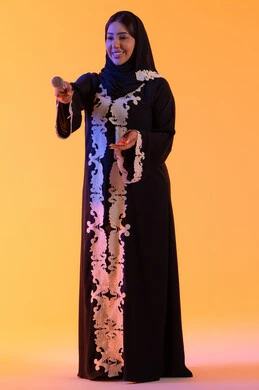 ممارسة موهبة الغناء، بورتريه لامراه عربيه خليجيه اماراتيه ترتدي العباءه المطرزة والحجاب تمسك بيدها المايكروفون ، سيده سعوديه تغني بإيماءات الحماس والسرور، تعابير الاندماج والتفاعل مع الموسيقي، تقديم العروض الصوتية ، تسجيل مقطع صوتي غنائي، تقديم البرامج الاذاعية، خلفية صفراء