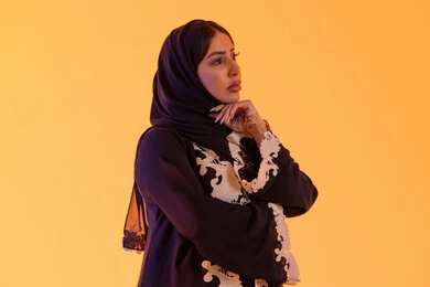 Anxiety and confusion in making the right decision, trying to find a solution to difficult problems, deep thinking and distraction, a portrait of an Arab Gulf Emirati woman wearing an abaya and hijab with her hand under her chin, a Saudi woman standing with gestures of integration.