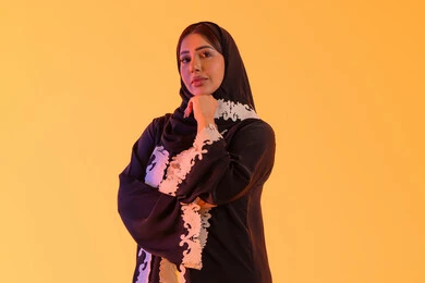 A portrait of an Arab Gulf Emirati woman wearing an abaya and hijab, resting her hand under her chin, showing anxiety and confusion in making the right decision, trying to find a solution to difficult problems, thinking deeply and lost in thought, a Saudi woman standing with gestures of integration.
