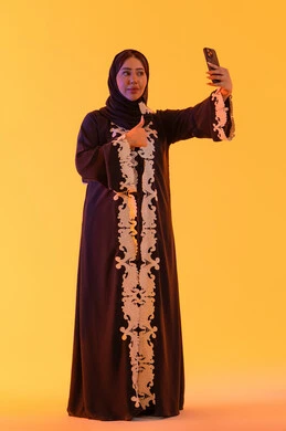 تعابير الموافقة والامتياز ، اجراء مكالمه فيديو ، الدردشة والتحدث مع الأصدقاء،تصفح مواقع وتطبيقات الانترنت، بورتريه لامراه عربيه خليجيه اماراتيه ترتدي العباءه والحجاب تمسك الجوال بيدها، سيده سعوديه تستخدم التقنيات والتكنولوجيا الحديثة بالحياة اليومية، خلفية صفراء