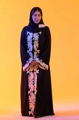 الاهتمام بالاناقة والاهتمام بالمظهر الخارجي، سيده سعوديه تنظر بتعابير السرور والسعاده ، بورتريه لامراه عربيه خليجيه اماراتيه ترتدي العباءه والحجاب تقف بايدي متشابكه وإيماءات الثقة بالنفس