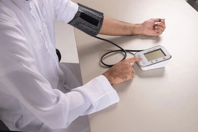 المتابعة الدورية لفحص الدم, بورتريه مقرب لرجل عربي خليجي اماراتي يرتدي الكندورة الاماراتية يقوم بقياس ضغط الدم باستخدام الميزان الالكتروني, مفهوم الطب والرعاية الصحية, العناية والاهتمام والحفاظ على الصحة, خلفية بيضاء