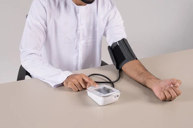 المتابعة الدورية لفحص الدم, بورتريه مقرب لرجل عربي خليجي اماراتي يرتدي الكندورة الاماراتية يقوم بقياس ضغط الدم باستخدام الميزان الالكتروني, مفهوم الطب والرعاية الصحية, العناية والاهتمام والحفاظ على الصحة, خلفية بيضاء