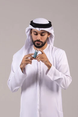 أجهزة استنشاق المخصصة للمرضى، المحافظة على ممر هوائي منتظم، مشاكل في الجهاز التنفسي، بورتريه لرجل عربي خليجي اماراتي يرتدي الكندورة والغترة الاماراتية يحمل بيده جهاز الرذاذ الخاص بمرض الربو، خلفية بيضاء