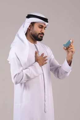 Inhalers designed for patients, maintaining an open airway, respiratory issues, a portrait of an Emirati Gulf Arab man wearing the kandura and Emirati ghutrah holding an asthma nebulizer in his hand, white background.
