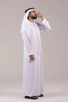 Maintaining a regular airway, respiratory problems, a portrait of an Emirati Gulf Arab man wearing the kandura and Emirati ghutrah holding an asthma nebulizer in his hand, inhalers designated for patients, full-body image, white background.