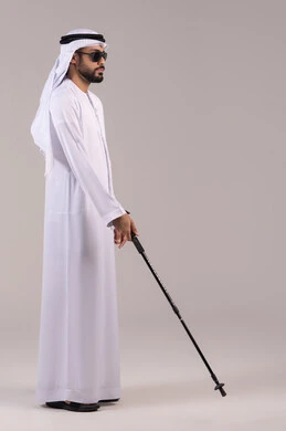 عدم القدرة على الرؤية، ضعف القدرة البصرية، بورتريه  لرجل عربي خليجي اماراتي كفيف يرتدي الكندورة والغترة ويضع النظارة الشمسية على عينه يمسك بيده عصا لمساعدته على الحركه الى المكان الصحيح، طول الجسم بالكامل، خلفيه بيضاء