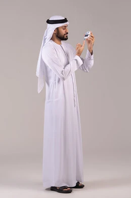 Problems of high blood sugar, diabetes, a portrait of a young Emirati Arab man wearing the kandura and the Emirati ghutrah checking his blood sugar level, modern electronic devices for rapid medical testing, full-body, white background.