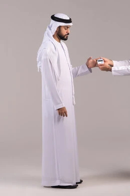 مشاكل ارتفاع السكر في الدم، الإصابة بداء السكري، بورتريه لشاب عربي خليجي اماراتي مريض يرتدي الكندورة والغترة الاماراتية يقوم بفحص نسبة السكر في دمه، أجهزة الكترونية حديثة للفحص الطبي السريع، الجسم بالطول الكامل, خلفية بيضاء