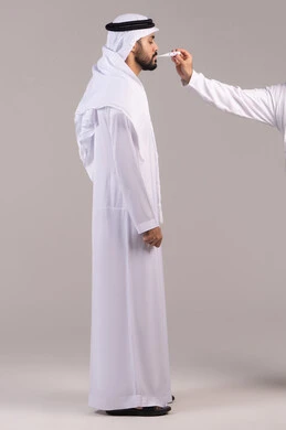 الشعور بالإرهاق والتعب وأعراض الحمى ، الحاجة إلى المساعدة الطبية, أهمية وجود ميزان رقمي في المنزل، بورتريه لرجل عربي خليجي اماراتي يرتدي الكندورة والغترة يمسك بيده جهاز مقياس الحرارة يقوم بقياس درجة حرارته, الجسم بالطول الكامل، خلفية بيضاء