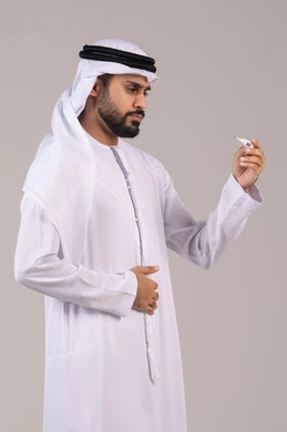 The importance of having a digital scale at home, feeling exhausted and tired with symptoms of fever, a portrait of an Emirati Gulf Arab man wearing a kandura and ghutrah holding a thermometer measuring his temperature, the need for medical assistance, white background.
