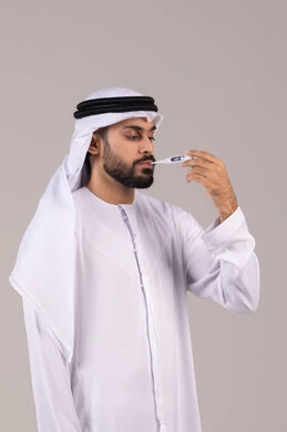 الحاجة إلى المساعدة الطبية, أهمية وجود ميزان رقمي في المنزل، الشعور بالإرهاق والتعب وأعراض الحمى ، بورتريه لرجل عربي خليجي اماراتي يرتدي الكندورة والغترة يمسك بيده جهاز مقياس الحرارة يقوم بقياس درجة حرارته, خلفية بيضاء