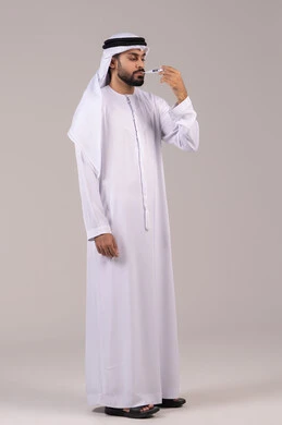 Feeling exhausted and tired with symptoms of fever, the need for medical assistance, the importance of having a digital thermometer at home, a portrait of an Emirati Gulf Arab man wearing a kandura and ghutrah holding a thermometer measuring his temperature, full-body, white background.