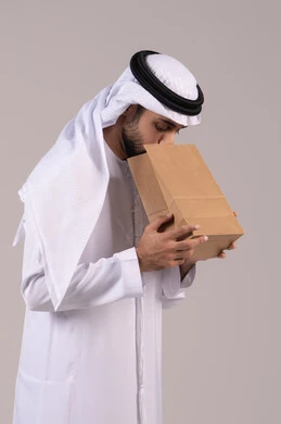 الإحساس بالمغص والوجع، الحاجه للمساعدة وطلب العلاج، الشعور بحرقة في المعدة وعسر الهضم، بورتريه لرجل عربي خليجي اماراتي يرتدي الكندورة الاماراتية والغترة البيضاء يحمل بيده كيس ورقي بإيماءات التقيؤ والغثيان، خلفية بيضاء