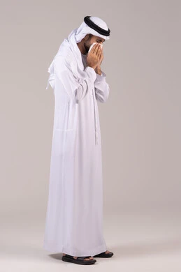 الشعور بالمرض و الزكام, التهاب الأنف و الجيوب التحسسية, الحاجة إلى العلاج والدواء, بورتريه من الجانب لرجل عربي خليجي إماراتي يرتدي الكندورة والغترة يضع منديل ورقي على وجهه بإيماءات العطاس, الجسم بالطول الكامل, خلفية بيضاء
