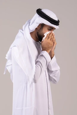 لزوم الذهاب إلى الطبيب، الشعور بالمرض و الزكام, التهاب الأنف و الجيوب التحسسية, الحاجة إلى العلاج والدواء, بورتريه من الجانب لرجل عربي خليجي إماراتي يرتدي الكندورة والغترة يضع منديل ورقي على وجهه بإيماءات العطاس, خلفية بيضاء