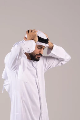 Stress and psychological pressure, a portrait of an Arab Gulf Emirati man wearing a kandura and ghutrah, placing his hands on his head and closing his eyes with gestures of severe pain, feeling of a migraine and headache, exhaustion and loss of concentration, feeling of headache and head pain, white background.