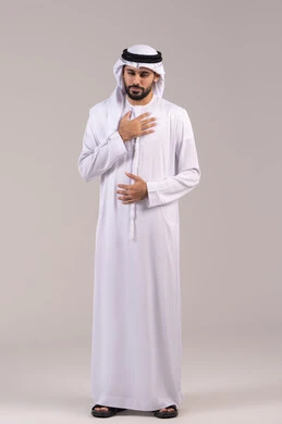 The feeling of chest pain, a portrait of a young Arab Gulf Emirati man wearing traditional attire with his hand on his chest, experiencing a bad state of tingling and pain, heart disorders and diseases, fatigue and exhaustion, and psychological stress, the necessity to go to the doctor for appropriate treatment, full body length, white background.