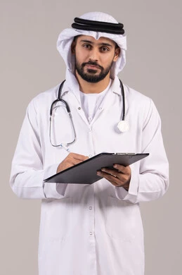 Writing prescriptions for patients, the concept of medicine and healthcare, working in the health sector in the UAE, standing upright with gestures of self-confidence, a portrait of an Arab Gulf Emirati doctor wearing a kandura and ghutrah and a medical coat, holding a stethoscope and looking at the camera, white background.