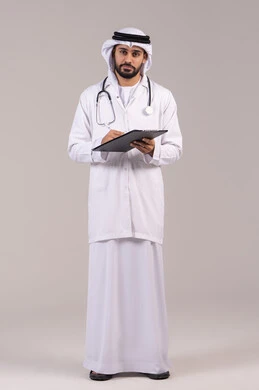 Writing patient reports, the concept of medicine and healthcare, working in the health sector in the UAE, standing upright with gestures of self-confidence, a portrait of an Arab Gulf Emirati doctor wearing the kandura and ghutrah and a medical coat, holding a stethoscope and looking at the camera, full body, white background.