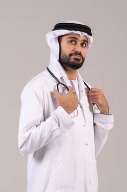 العمل في القطاع الصحي في الامارات، الفحص الطبي وتقديم الخدمات العلاجية للمرضى, الوقوف باستقامة بإيماءات الثقة بالنفس، بورتريه لطبيب عربي خليجي اماراتي يرتدي الكندورة والغترة والمعطف الطبي يضع السماعة الطبية ينظر إلى شيء ما في الاعلى، خلفية بيضاء