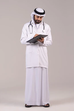 حسن التعامل مع المراجعين، تدوين نتائج الفحوصات بالسجل الطبي، مفهوم الطب والرعاية الصحية، العمل في القطاع الصحي, بورتريه لطبيب عربي خليجي اماراتي يرتدي الكندورة والغترة والمعطف الطبي يضع السماعة الطبية يقوم بكتابة تقارير المرضى، الطول الكامل للجسم، خلفية بيضاء