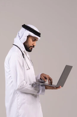 العمل في القطاع الصحي، تقديم الاستشارات الطبية عن طريق الإنترنت، استخدام الأجهزة التقنية الحديثة في الطب، بورتريه من الجانب لطبيب عربي خليجي اماراتي يرتدي الكندورة والغترة والمعطف الأبيض يحمل بيده الحاسوب المحمول، خلفية بيضاء