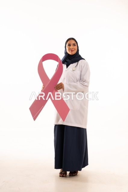 Clarifying the importance of early detection in October, the concept of medicine and healthcare, a portrait of an Arab Gulf Saudi female doctor wearing an abaya and a white apron holding a flag with the breast cancer awareness symbol, a pink ribbon in awareness campaigns, white background.