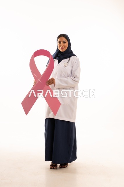Clarifying the importance of early detection in October, the concept of medicine and healthcare, a portrait of an Arab Gulf Saudi female doctor wearing an abaya and a white apron holding a flag with the breast cancer awareness symbol, a pink ribbon in awareness campaigns, white background.