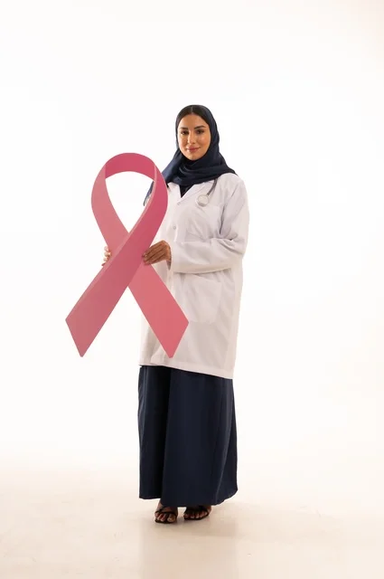 توضيح أهمية الفحص المبكر في شهر أكتوبر، مفهوم الطب والرعاية الصحية ، بورتريه لطبيبة عربية خليجية سعودية ترتدي العباءة والمئزر الأبيض تمسك بيديها علم عليه رمز التوعية بسطان الثدي، شريط وردي في حملات التوعية, خلفية بيضاء