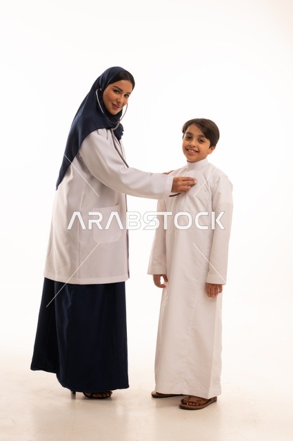 العمل في القطاع الصحي في السعودية، القيام بالرعاية الصحية والاهتمام بصحة المرضى، بورتريه  لطبيبة عربية خليجية سعودية ترتدي عباءة ومئزر أبيض تقوم بفحص طفل عبر سماعة الأذن، استخدام سماعة الطبيب لسماع نبضات القلب، الاهتمام بالصحة الجسدية