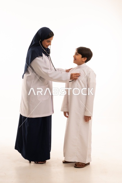 العمل في القطاع الصحي في السعودية، القيام بالرعاية الصحية والاهتمام بصحة المرضى، بورتريه  لطبيبة عربية خليجية سعودية ترتدي عباءة ومئزر أبيض تقوم بفحص طفل عبر سماعة الأذن، استخدام سماعة الطبيب لسماع نبضات القلب، الاهتمام بالصحة الجسدية