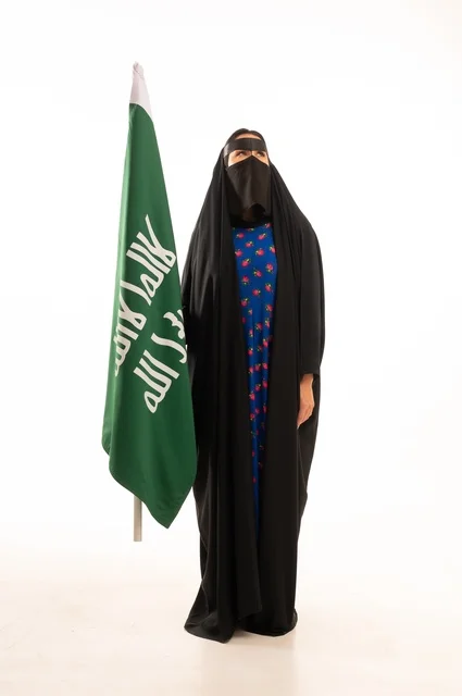 Wearing traditional attire on national occasions, commemorating the Day of Foundation 1727 AD, the establishment of the first Saudi state on February 22, a portrait of an Arab Gulf Saudi woman wearing a burqa and abaya holding the flag and emblem of the Day of Foundation with expressions of pride and honor, full body length, white background.