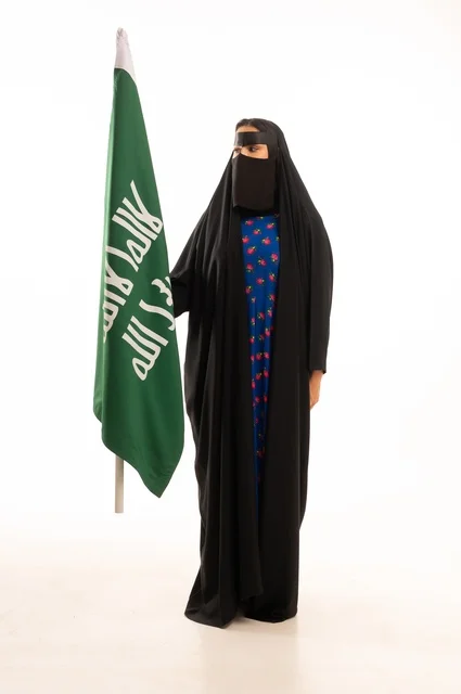 Wearing traditional attire on national occasions, commemorating the Day of Foundation 1727 AD, the establishment of the first Saudi state on February 22, a portrait of an Arab Gulf Saudi woman wearing a burqa and abaya holding the flag and emblem of the Day of Foundation with expressions of pride and honor, full body length, white background.