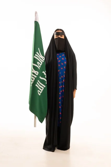 Wearing traditional attire on national occasions, commemorating the Day of Foundation 1727 AD, the establishment of the first Saudi state on February 22, a portrait of an Arab Gulf Saudi woman wearing a burqa and abaya holding the flag and emblem of the Day of Foundation with expressions of pride and honor, full body length, white background.