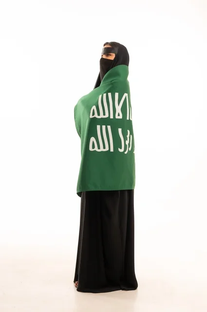 The establishment of the first Saudi state on February 22, wearing traditional costumes on national occasions, the anniversary of our beginning in 1727 AD, a portrait of a Gulf Arab Saudi woman wearing a niqab and an abaya, draped with a flag and the emblem of the Foundation Day, expressing pride and honor, full body length, white background.