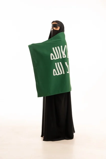 The establishment of the first Saudi state on February 22, wearing traditional costumes on national occasions, the anniversary of our beginning in 1727 AD, a portrait of a Gulf Arab Saudi woman wearing a niqab and an abaya, draped with a flag and the emblem of the Foundation Day, expressing pride and honor, full body length, white background.