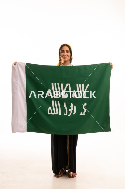 الاحتفال بالمناسبات والأعياد الوطنية الشعبية، ذكرى تأسيس الدولة السعودية الأولى 22 فبراير، يوم بدينا 1727 م، ارتداء أزياء المنطقة الوسطى، بورتريه لإمرأة عربية خليجية سعودية مبتسمة ترتدي الكرتة والهامة تحمل بيدها علم يوم التأسيس، الجسم بالطول الكامل، خلفية بيضاء