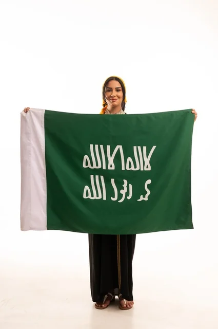 الاحتفال بالمناسبات والأعياد الوطنية الشعبية، ذكرى تأسيس الدولة السعودية الأولى 22 فبراير، يوم بدينا 1727 م، ارتداء أزياء المنطقة الوسطى، بورتريه لإمرأة عربية خليجية سعودية مبتسمة ترتدي الكرتة والهامة تحمل بيدها علم يوم التأسيس، الجسم بالطول الكامل، خلفية بيضاء