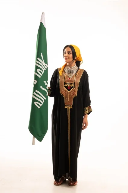 الاحتفال بالمناسبات والأعياد الوطنية الشعبية، ذكرى تأسيس الدولة السعودية الأولى 22 فبراير، يوم بدينا 1727 م، ارتداء أزياء المنطقة الوسطى، بورتريه لإمرأة عربية خليجية سعودية مبتسمة ترتدي الكرتة والهامة تحمل بيدها علم يوم التأسيس، الجسم بالطول الكامل، خلفية بيضاء