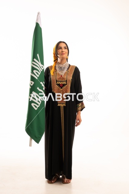 Celebrating popular national occasions and holidays, the anniversary of the establishment of the first Saudi state on February 22, the day we began in 1727 AD, wearing the traditional attire of the central region, a portrait of a smiling Saudi Gulf Arab woman wearing the kurta and headscarf holding the flag of the Foundation Day in her hand, full-body, white background.