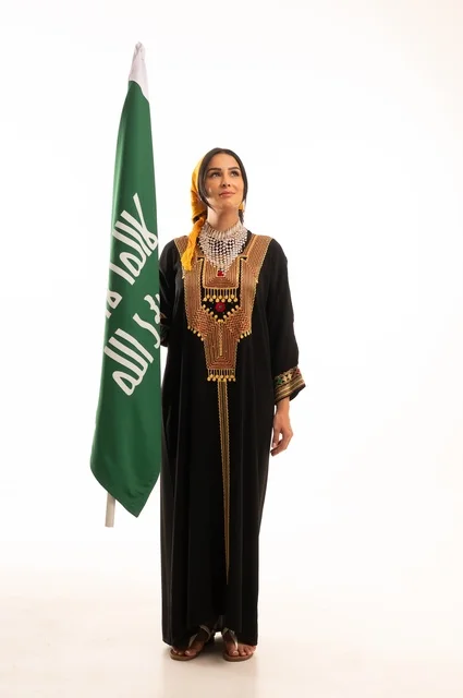 الاحتفال بالمناسبات والأعياد الوطنية الشعبية، ذكرى تأسيس الدولة السعودية الأولى 22 فبراير، يوم بدينا 1727 م، ارتداء أزياء المنطقة الوسطى، بورتريه لإمرأة عربية خليجية سعودية مبتسمة ترتدي الكرتة والهامة تحمل بيدها علم يوم التأسيس، الجسم بالطول الكامل، خلفية بيضاء