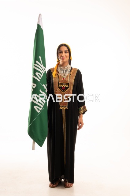 الاحتفال بالمناسبات والأعياد الوطنية الشعبية، ذكرى تأسيس الدولة السعودية الأولى 22 فبراير، يوم بدينا 1727 م، ارتداء أزياء المنطقة الوسطى، بورتريه لإمرأة عربية خليجية سعودية مبتسمة ترتدي الكرتة والهامة تحمل بيدها علم يوم التأسيس، الجسم بالطول الكامل، خلفية بيضاء