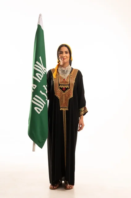 الاحتفال بالمناسبات والأعياد الوطنية الشعبية، ذكرى تأسيس الدولة السعودية الأولى 22 فبراير، يوم بدينا 1727 م، ارتداء أزياء المنطقة الوسطى، بورتريه لإمرأة عربية خليجية سعودية مبتسمة ترتدي الكرتة والهامة تحمل بيدها علم يوم التأسيس، الجسم بالطول الكامل، خلفية بيضاء