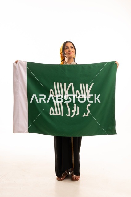 ارتداء أزياء المنطقة الوسطى، الاحتفال بالمناسبات والأعياد الوطنية الشعبية، ذكرى تأسيس الدولة السعودية الأولى 22 فبراير، يوم بدينا 1727 م، بورتريه لإمرأة عربية خليجية سعودية مبتسمة ترتدي الكرتة والهامة تحمل بيدها علم يوم التأسيس، الجسم بالطول الكامل، خلفية بيضاء